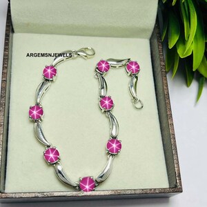 May include: A silver bracelet featuring pink star-shaped gemstones. The bracelet is displayed in a box with the inscription "ARGEMSNJEWELS" inside.