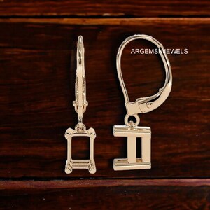 May include: A pair of gold-tone earring settings with a rectangular shape. The settings are designed to hold a gemstone or other embellishment. The earrings have a lever back closure.