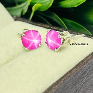 Op de afbeelding: Een paar zilveren oorbelletjes met roze ster-saffieren. De oorbellen zijn gezet in een eenvoudig, elegant ontwerp.