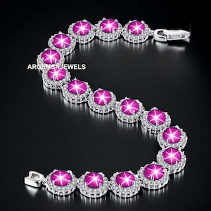 May include: A silver bracelet featuring star-shaped, magenta gemstones surrounded by a halo of small, clear stones. The bracelet is set against a black background, with the text "ARGEMSN JEWELS" visible.