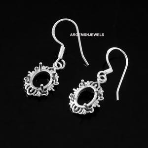 May include: A pair of silver earrings with a delicate, ornate design. Each earring features a round, open setting for a gemstone or other embellishment. The earrings have a simple, elegant style.