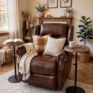 May include: A dark brown leather recliner chair featuring a plaid orange pillow and a textured cream pillow. A cream-colored throw blanket is draped over the arm. Two round wooden side tables with black metal bases stand on either side.