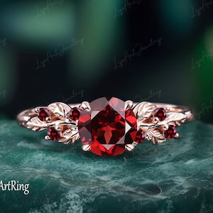 Könnte beinhalten: Ein Ring aus Roségold mit einem großen roten Edelstein, umgeben von kleineren roten Edelsteinen und blattförmigen Akzenten.