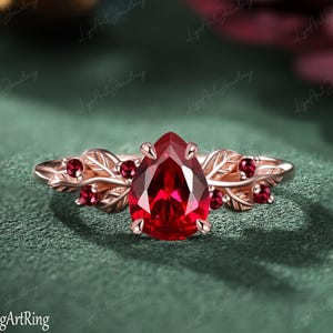 Op de afbeelding: Roségouden ring met een peervormige, dieprode edelsteen. De ring is versierd met blad- en bessenaccenten, en kleinere rode edelstenen. De band heeft een delicaat, door de natuur geïnspireerd ontwerp.