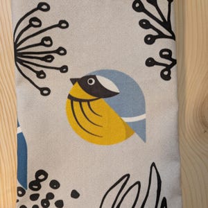 May include: A gray fabric with a stylized blue and yellow bird design. The bird has a black eye and a black beak. The background is a light gray with black floral designs.