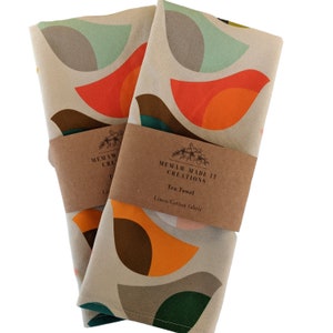 Pu&ograve; includere: Due asciugamani da t&egrave; con un motivo geometrico di cerchi sovrapposti in tonalit&agrave; di arancione, marrone, verde e blu su uno sfondo beige. Gli asciugamani sono etichettati con "Memaw Made It Creations" e "Tea Towel" con il tessuto indicato come "Linen/Cotton fabric".