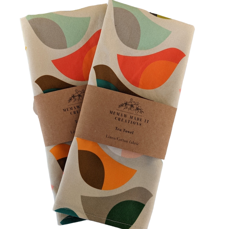 Pu&ograve; includere: Due asciugamani da t&egrave; con un motivo geometrico di cerchi sovrapposti in tonalit&agrave; di arancione, marrone, verde e blu su uno sfondo beige. Gli asciugamani sono etichettati con "Memaw Made It Creations" e "Tea Towel" con il tessuto indicato come "Linen/Cotton fabric".