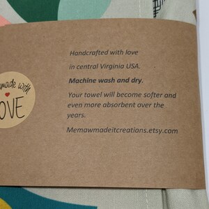 Pu&ograve; includere: Un'etichetta di carta marrone con testo bianco che recita "Handcrafted with love in central Virginia USA. Machine wash and dry. Your towel will become softer and even more absorbent over the years. Memawmadeitcreations.etsy.com". L'etichetta &egrave; attaccata a un tessuto verde chiaro e bianco con un motivo geometrico.