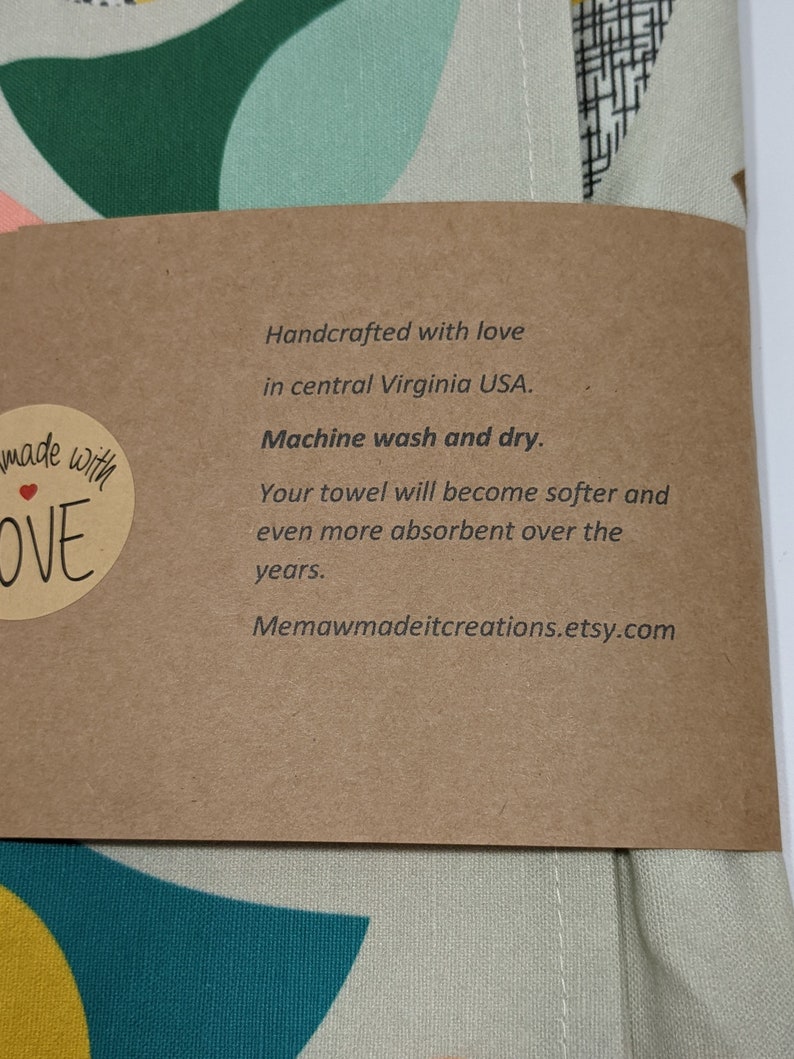 Pu&ograve; includere: Un'etichetta di carta marrone con testo bianco che recita "Handcrafted with love in central Virginia USA. Machine wash and dry. Your towel will become softer and even more absorbent over the years. Memawmadeitcreations.etsy.com". L'etichetta &egrave; attaccata a un tessuto verde chiaro e bianco con un motivo geometrico.