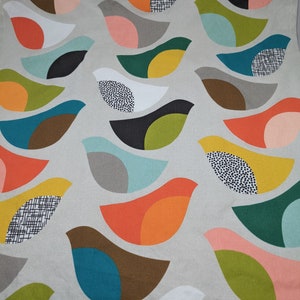 Pu&ograve; includere: Un tessuto con un motivo ripetitivo di uccelli stilizzati in vari colori, tra cui turchese, arancione, giallo, verde, marrone, rosa e bianco. Gli uccelli sono disposti a forma di onda.