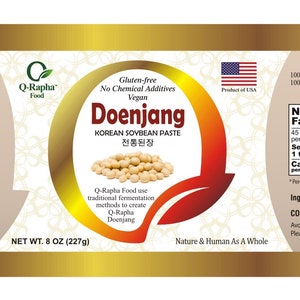 K&ouml;nnte beinhalten: Ein goldenes Etikett mit einer rot-wei&szlig;en amerikanischen Flagge, einem wei&szlig;en Hintergrund mit einem floralen Muster und dem Text "Q-Rapha Doenjang is..." und "Doenjang KOREAN SOYBEAN PASTE 전통된장". Das Etikett enth&auml;lt auch den Text "Gluten free No Chemical Additives Vegan" und "NET WT. 8 OZ (227g)".