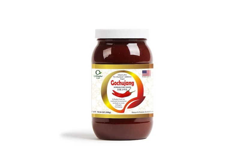Op de afbeelding: Een glazen pot met rode Gochujang Koreaanse Chillisauce met een wit deksel. Het etiket is goudkleurig met een groen bladerenontwerp en de tekst "Gochujang Korean Chili Sauce" in zwart. De pot is 535 g (18,94 oz).