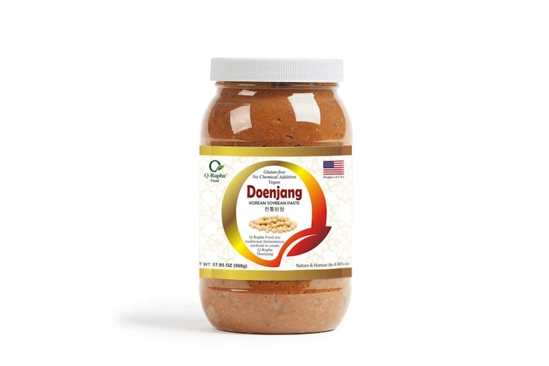 May include: A glass jar of Doenjang Korean Soybean Paste, a fermented soybean paste, with a gold label that reads "Doenjang Korean Soybean Paste" and "Gluten Free No Chemical Additives Vegan". The jar is 17.65 oz (500g) and is made in the USA.