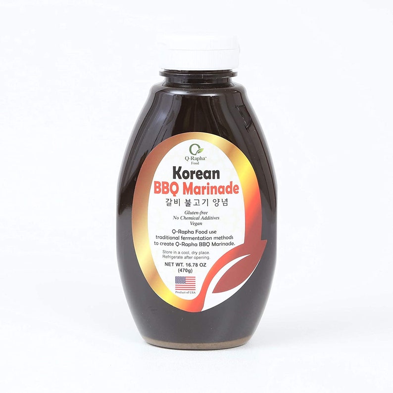 May include: A glass bottle of Q-Rapha Korean BBQ Marinade, a gluten-free, vegan marinade with no chemical additives. The label is gold with black text and features the words "Korean BBQ Marinade" and "갈비 불고기 양념". The bottle is 16.78 ounces (470 grams).