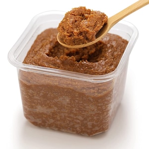 May include: A close-up of a container of brown miso paste with a spoonful of miso being lifted out of the container.