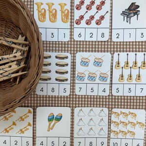 May include: A collection of flashcards featuring musical instruments, including tubas, violins, a piano, tambourines, drums, guitars, maracas, triangles, and French horns. Each card displays a different number of instruments, with numbers below each image.