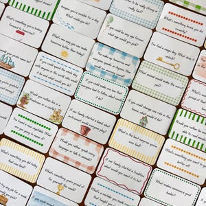 May include: A set of white cards featuring questions like "What is your biggest dream?" and "What would you do if you were invisible for a day?" The cards have decorative borders in green, blue, and yellow. The cards are designed for a game.