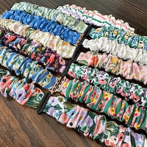 Puede incluir: Una colección de correas de reloj de tela coloridas con patrones florales y geométricos. Las correas están hechas de tela suave y elástica y están diseñadas para adaptarse al Apple Watch.