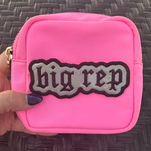 Op de afbeelding: Een felroze ritsvakje met een zwart en zilveren patch waarop in gotische letters "big rep" staat.