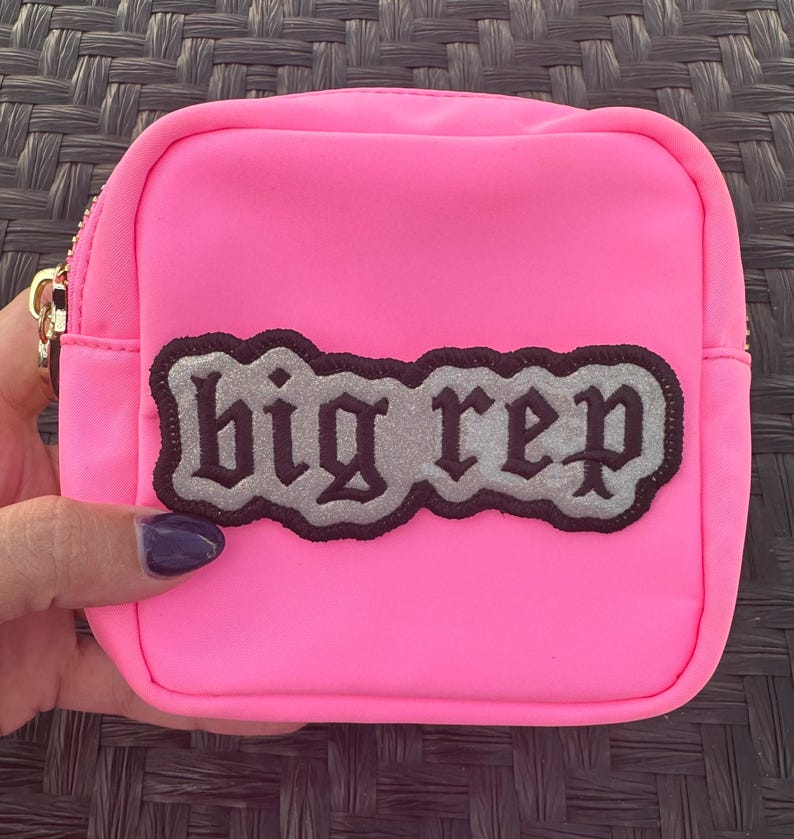 Op de afbeelding: Een felroze ritsvakje met een zwart en zilveren patch waarop in gotische letters "big rep" staat.