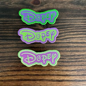 May include: Three purple and green felt patches with the word "Dopey" embroidered in green. The patches are stitched around the edges.