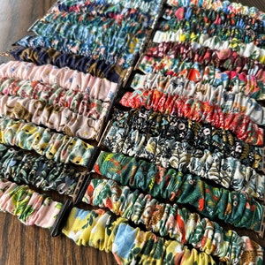 May include: A collection of colorful patterned watch bands, featuring a variety of floral and geometric designs. The bands are made of fabric and are designed to fit Apple Watches.