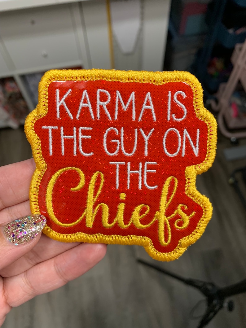 May include: Red and gold embroidered patch with the text "Karma is the guy on the Chiefs" in white.