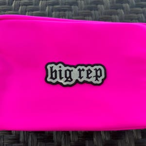 Op de afbeelding: Een felroze ritsvak met een zwart en zilveren patch waarop "big rep" staat