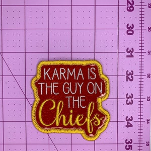 May include: A red and gold embroidered patch with the text "KARMA IS THE GUY ON THE CHIEFS" in white lettering.