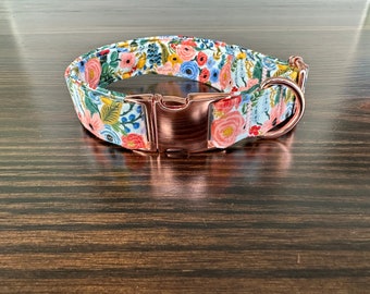 May include: A floral dog collar with a rose gold buckle and D-ring. The collar is made of a white fabric with a floral pattern in shades of pink, blue, and green.