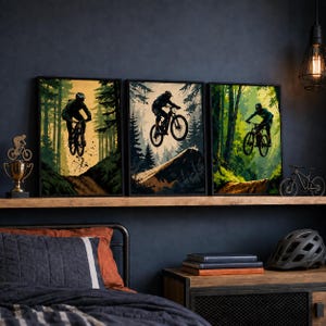 Puede incluir: Un conjunto de tres l&aacute;minas de arte mural enmarcadas que representan ciclistas de monta&ntilde;a saltando en un bosque, acompa&ntilde;ado de un trofeo dorado con silueta de bicicleta y un casco de bicicleta negro sobre una superficie de madera.