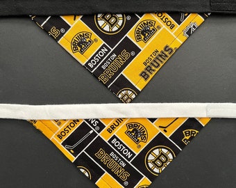 May include: Two triangular bandanas with a Boston Bruins logo pattern in black, gold, and white. The bandanas have a black and white strap. The bandanas are likely for a pet.