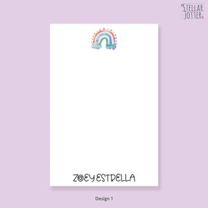 May include: A white notepad with a rainbow and clouds design at the top. The notepad has the text "ZOEY ESTRELLA" at the bottom and the words "STELLAR JOTTER" in the top right corner.