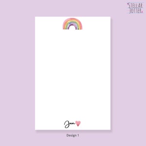 May include: A white notepad with a rainbow and a pink heart. The notepad has the text "Stellar Jotter" and "Design 1" printed on it.