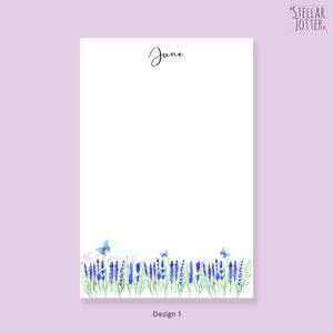 May include: A white notepad with the word "June" in cursive. The bottom border features a watercolour design of lavender and butterflies. The notepad is labelled "Design 1" and has the Stellar Jotter logo in the top right corner.
