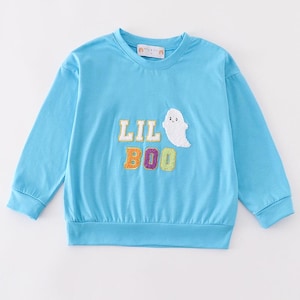 Może przedstawiać: Błękitna bluza z długim rękawem z haftowanymi słowami "LIL BOO" w kolorowych literach i białą aplikacją ducha. Bluza ma okrągły dekolt oraz ściągacze przy mankietach i u dołu. Top z motywem Halloween.