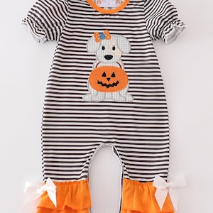 May include: A brown and white striped baby onesie with a white dog holding a pumpkin with a jack-o-lantern face. The onesie has orange ruffles at the bottom and white bows on the sides.