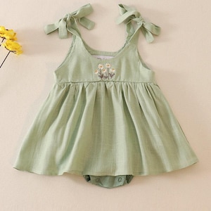 May include: A green sleeveless baby dress with a floral embroidery design and tie straps.