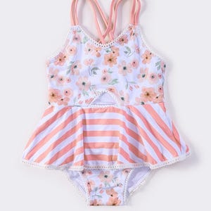 May include: A child's swimsuit with a floral top and a striped skirted bottom. The top has a keyhole and crisscross straps. The swimsuit is white, peach, and pink. The measurements are in centimetres.