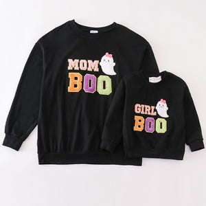 Może przedstawiać: Czarne bluzy z długimi rękawami z duchem i tekstem. Większa bluza ma napis "MOM BOO", a mniejsza "GIRL BOO".