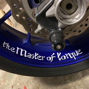 Può includere: Una ruota di moto blu con un pneumatico nero e un adesivo bianco che dice "the Master of Torque".