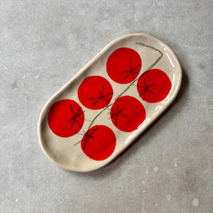 Peut inclure: Plat ovale en céramique avec une base crème. Le plat est décoré de six illustrations de tomates rouge vif, chacune avec un motif en étoile noir, reliées par une tige verte. Idéal pour servir des entrées ou de petits plats.