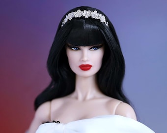 May include: A fashion doll with black hair, blue eyes, and red lipstick. The doll wears a black sequined dress with a white bow and a silver tiara. The doll is wearing light blue gloves.