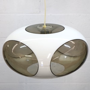 May include: A white and brown pendant light fixture. The light has a rounded, oval shape with a white body and three brown, oval-shaped lenses. The light hangs from a thin, off-white cord.