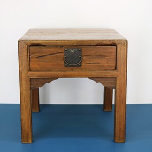 May include: A small wooden table with a single drawer and a metal handle. The table has a dark brown finish and sits on four legs.