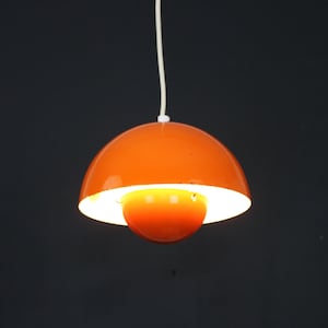 Könnte beinhalten: Eine leuchtend orangefarbene Pendelleuchte mit einem weißen Innenschirm. Die Lampe ist eingeschaltet und beleuchtet den Raum.