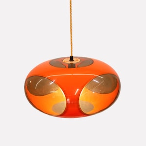 May include: A retro-style orange pendant light with a gold-colored cord. The light fixture has a rounded, oval shape with gold-colored accents and a glossy finish. This mid-century modern lighting fixture is suspended from the ceiling.