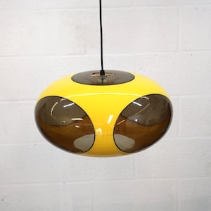 May include: A retro-style pendant light fixture. The light has a bright yellow, rounded body with dark brown, oval-shaped accents. A dark cord suspends the light from the ceiling. The fixture is a unique, eye-catching design.