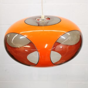 May include: Orange and gray retro pendant light fixture. The mid-century modern lamp has a rounded shape with a central orange section and gray and red accents. The light hangs from a white cord.
