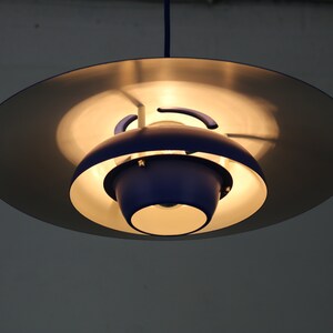 Op de afbeelding: Een blauwe en zilveren hanglamp met een ronde, schotelvormige kap.